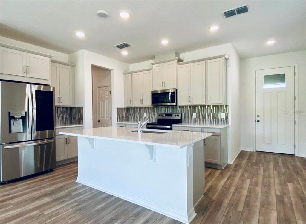 A kitchen features light-colored cabinets, a white island, stainless steel appliances, and wood-look flooring — 2668 SPIDER LILY COURT, CLERMONT, FL