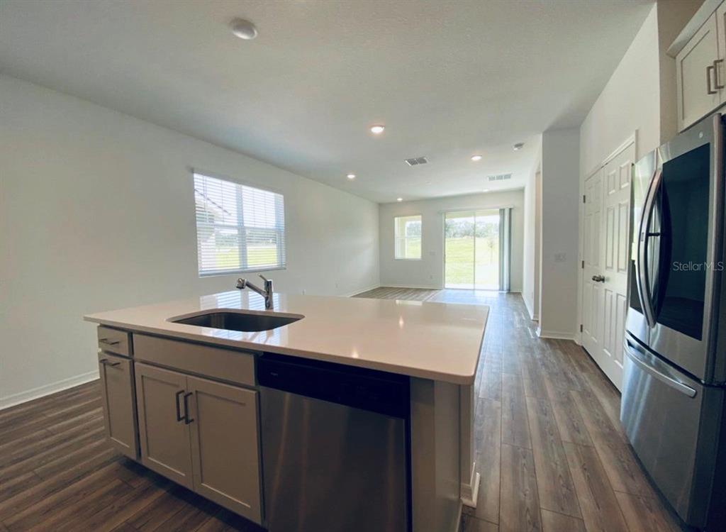 A kitchen island with a sink and dishwasher faces an open-concept living area with flooring — 2668 SPIDER LILY COURT, CLERMONT, FL