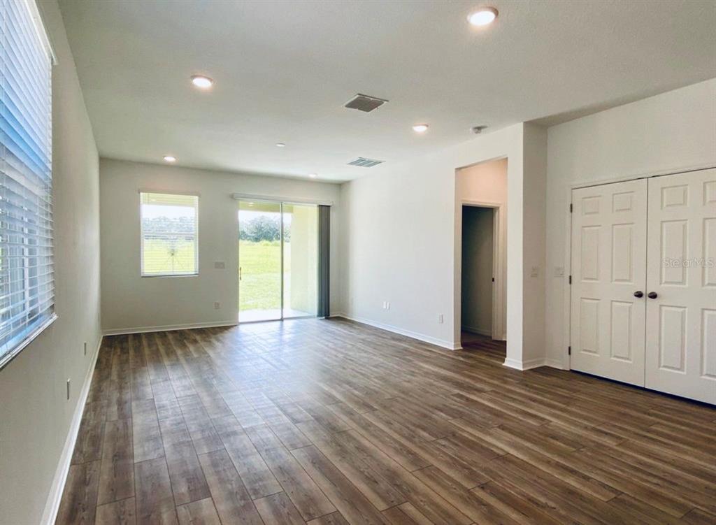An empty living room features wood-look flooring, white walls, recessed lighting, and sliding glass doors — 2668 SPIDER LILY COURT, CLERMONT, FL