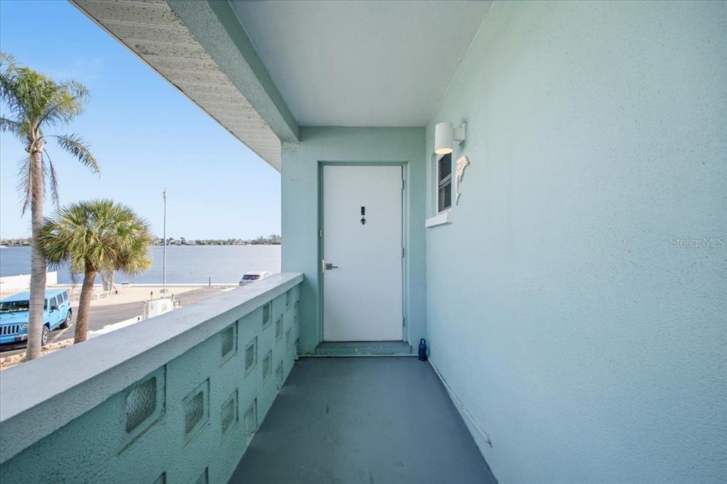 An exterior balcony with a white door overlooks a body of water and palm trees — 611 GULF DRIVE N UNIT C29, BRADENTON BEACH, FL
