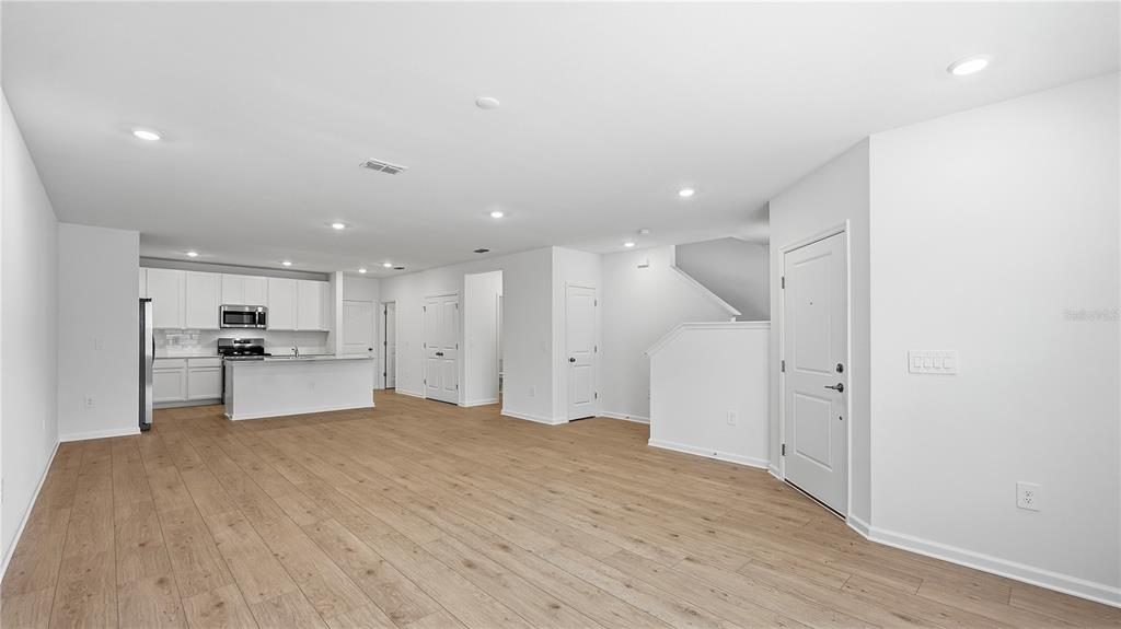 An open-concept kitchen and living area features white cabinetry, stainless steel appliances, and wood-look flooring — 5120 CLAY WHALEY ROAD, ST CLOUD, FL