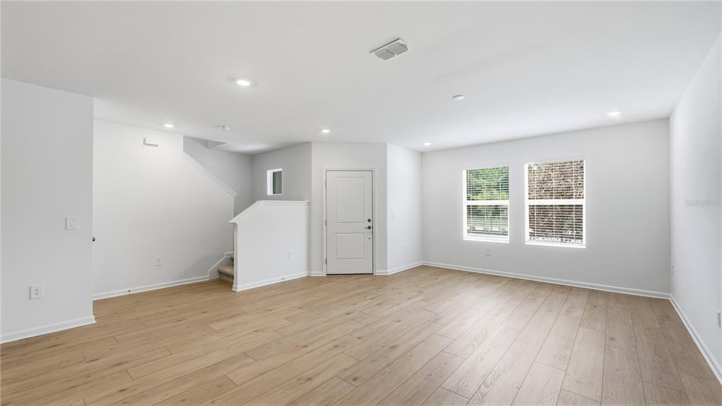 An empty living room features light wood-look flooring, white walls, recessed lighting, and a staircase — 5120 CLAY WHALEY ROAD, ST CLOUD, FL
