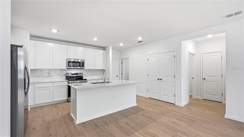 A modern kitchen features white cabinets, stainless steel appliances, a center island, and wood flooring — 5120 CLAY WHALEY ROAD, ST CLOUD, FL