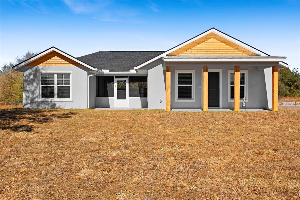 A single-story house with gray stucco siding, wood-trimmed gables, and a covered front porch — 20806 NW 274TH STREET, OKEECHOBEE, FL