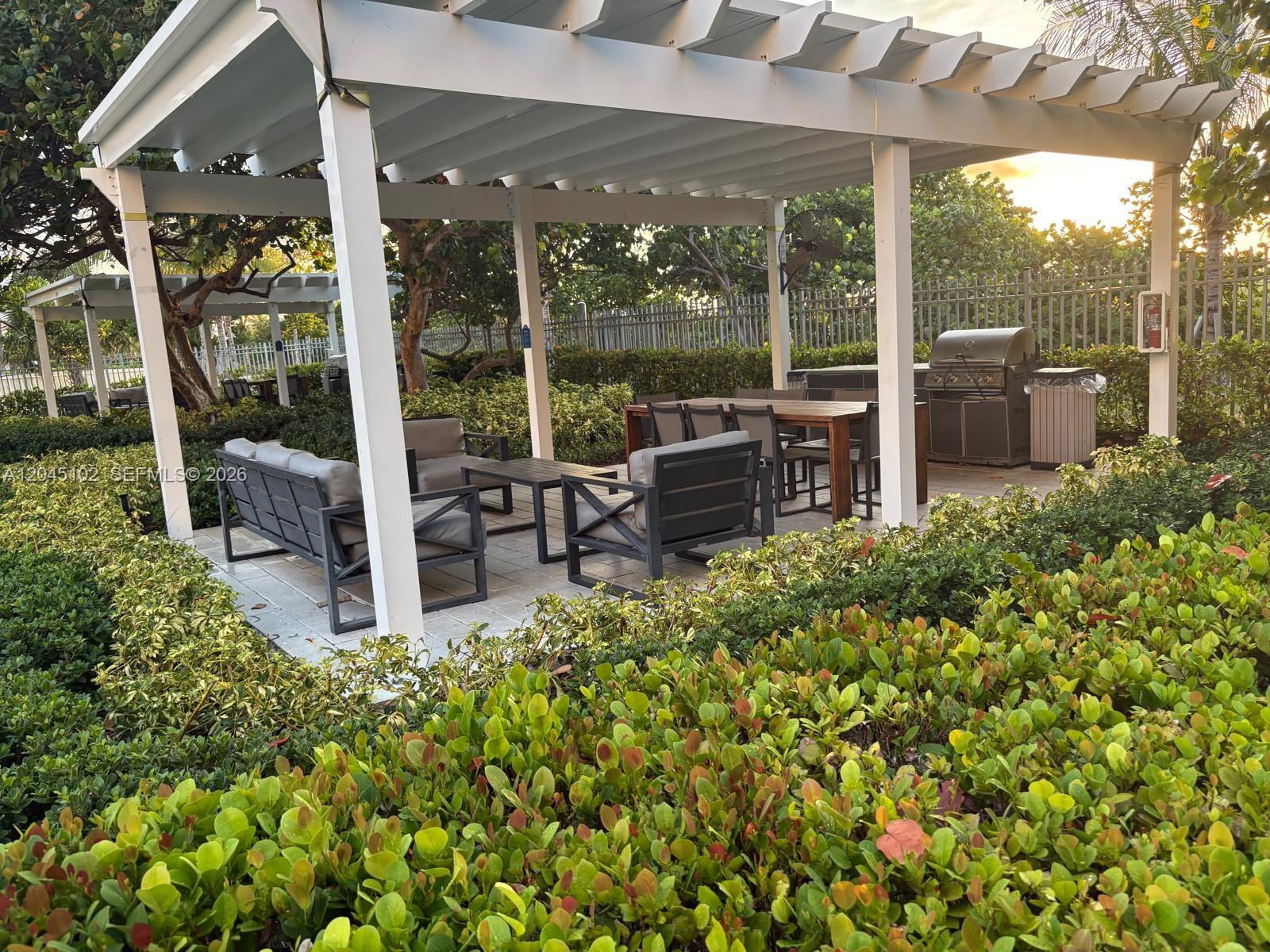 An outdoor patio area features a white pergola, lounge seating, a dining table, and a grill — 199 Ocean Lane Dr # 113, Key Biscayne FL 33149, KEY BISCAYNE, FL