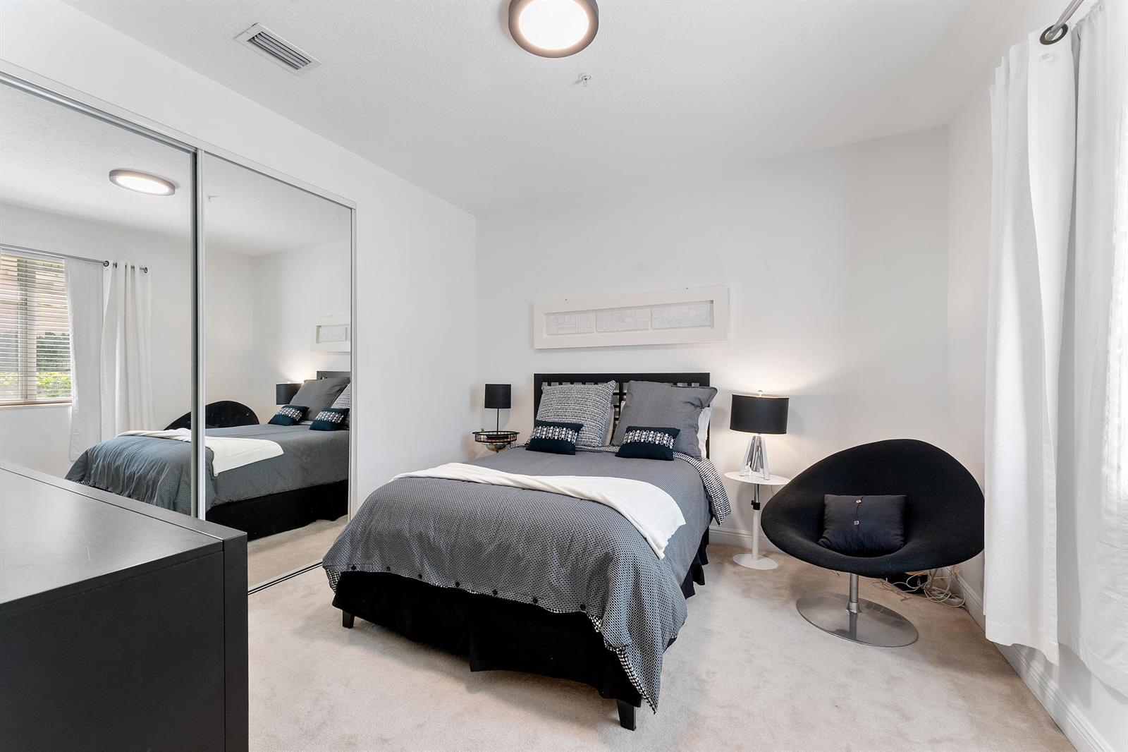 A bedroom features a bed with grey bedding, a black accent chair, and mirrored closets — 638 NW 38th Circle, Boca Raton FL 33431, BOCA RATON, FL