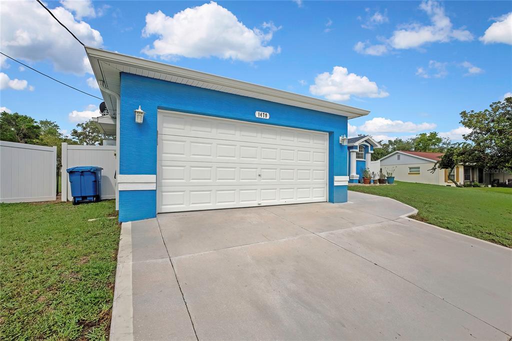 A blue house exterior features a white two-car garage door and a concrete driveway — 1479 PIPER ROAD, SPRING HILL, FL