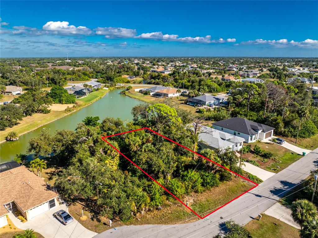 An aerial view shows a vacant, wooded residential lot outlined in red next to a lake — 106 REBEL COURT, ROTONDA WEST, FL