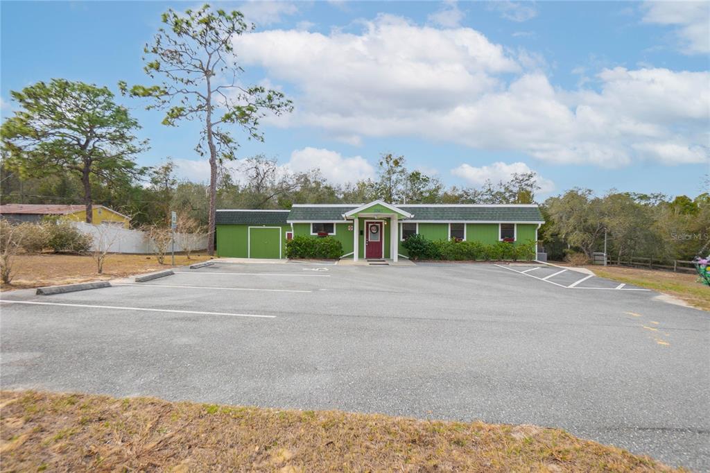 A green single-story building with a dark shingled roof sits behind a paved parking lot — 11840 N ANGUS HILLS TERRACE, DUNNELLON, FL