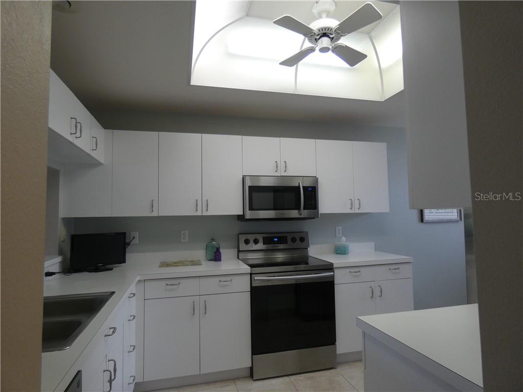 A kitchen features white cabinets, stainless steel appliances, white countertops, and a ceiling fan — 8735 OLDE HICKORY AVENUE UNIT 8101, SARASOTA, FL