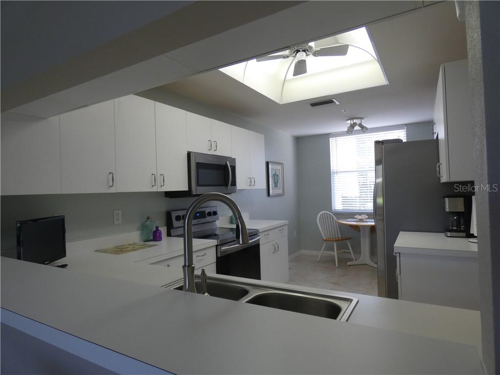 A kitchen with white cabinets, stainless steel appliances, a breakfast nook, and a ceiling skylight — 8735 OLDE HICKORY AVENUE UNIT 8101, SARASOTA, FL