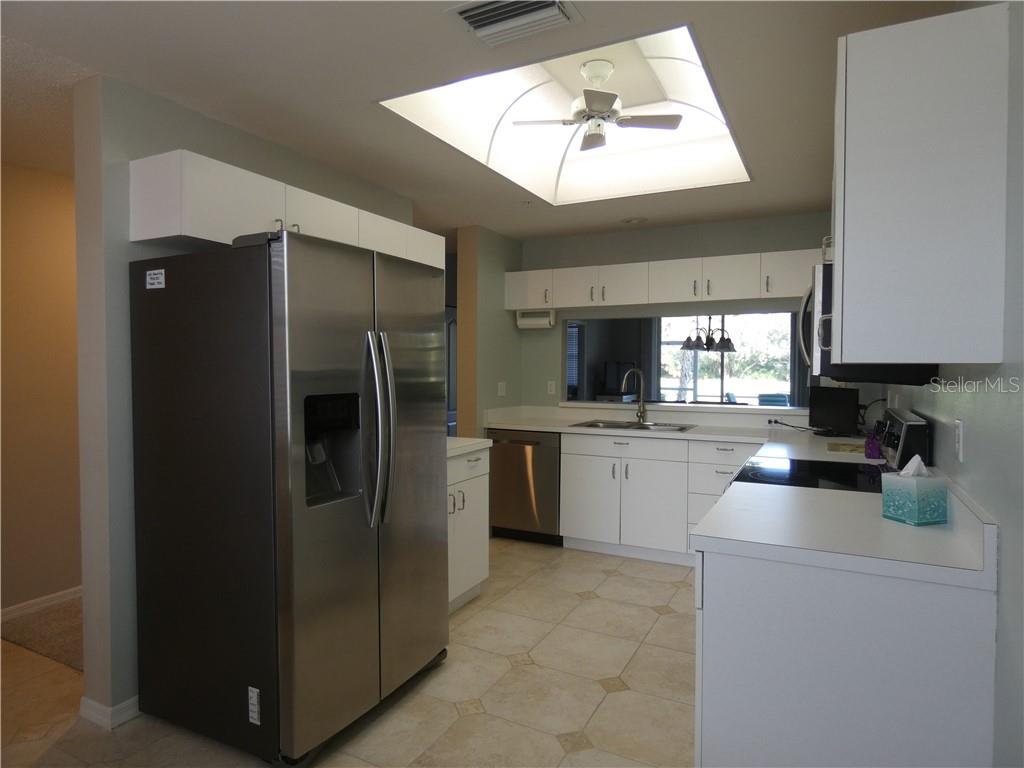 A kitchen features white cabinets, stainless steel appliances, tile flooring, and a large ceiling skylight — 8735 OLDE HICKORY AVENUE UNIT 8101, SARASOTA, FL