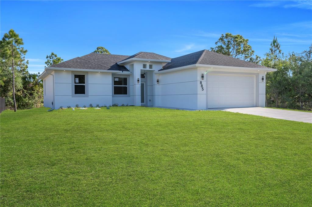 A single-story white house with a two-car garage and a large green lawn — 885 BARCIA STREET E, LEHIGH ACRES, FL