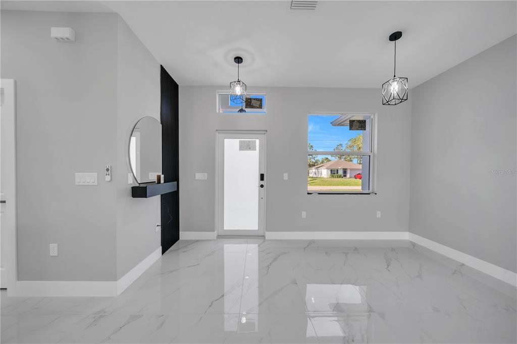 A bright entryway features white marble floors, a black accent wall, and two pendant lights — 885 BARCIA STREET E, LEHIGH ACRES, FL