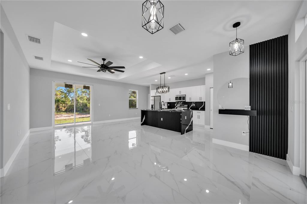 A modern open-concept kitchen and living area with white marble floors and black accent walls — 885 BARCIA STREET E, LEHIGH ACRES, FL