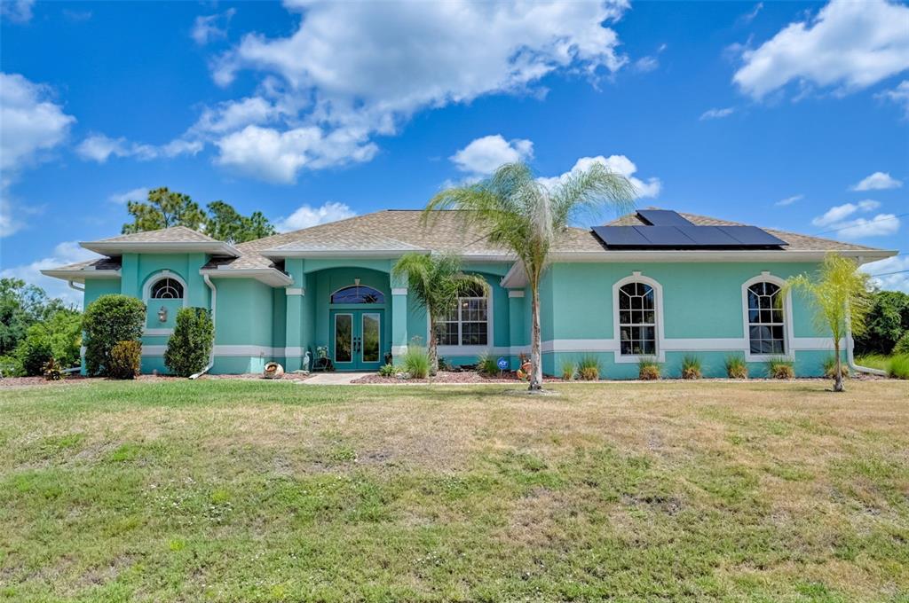 A teal, single-story house with a shingled roof, solar panels, and a front lawn — 2459 JOHANNESBERG ROAD, NORTH PORT, FL