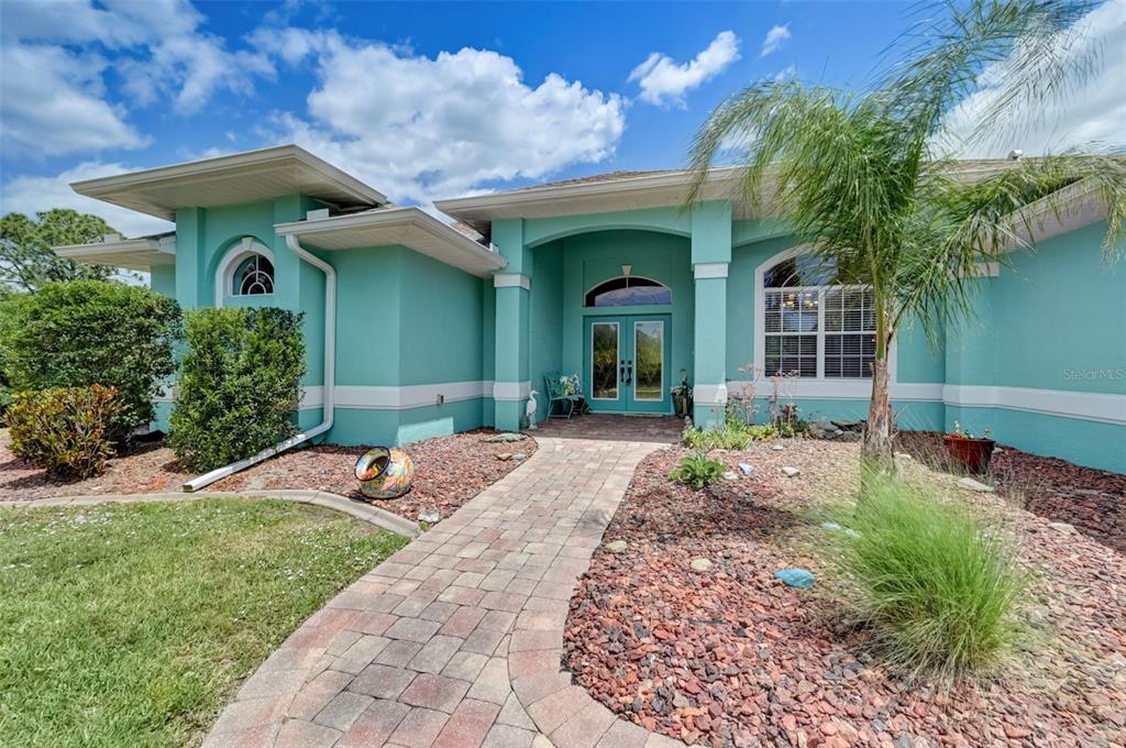 A teal house with a brick walkway leading to a double-door entryway under a portico — 2459 JOHANNESBERG ROAD, NORTH PORT, FL