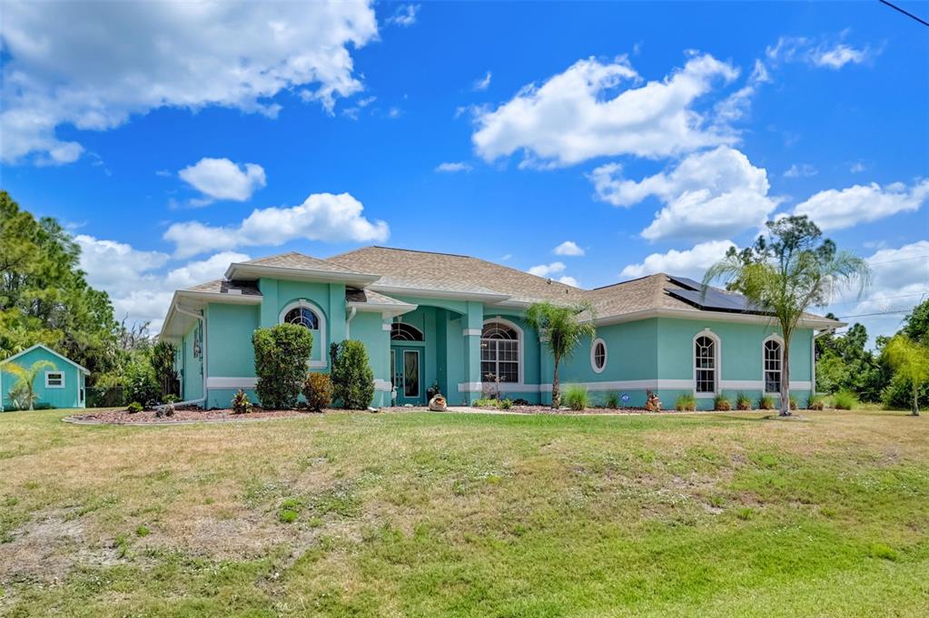 A teal single-story house with a tan roof and a detached shed sits on grass — 2459 JOHANNESBERG ROAD, NORTH PORT, FL
