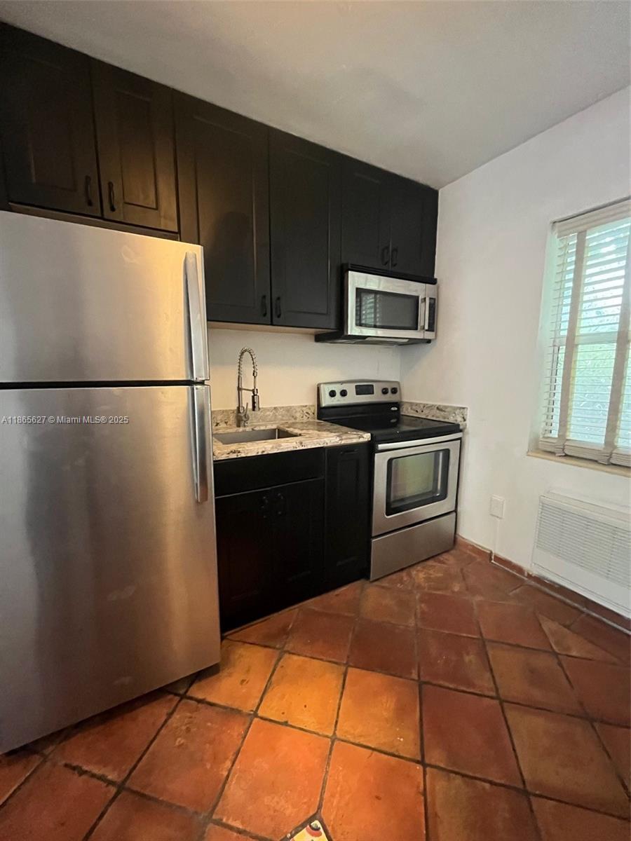 A kitchen features dark cabinets, stainless steel appliances, granite countertops, and terracotta tile flooring — 645 NE 77th St # 6, Miami FL 33138, MIAMI, FL