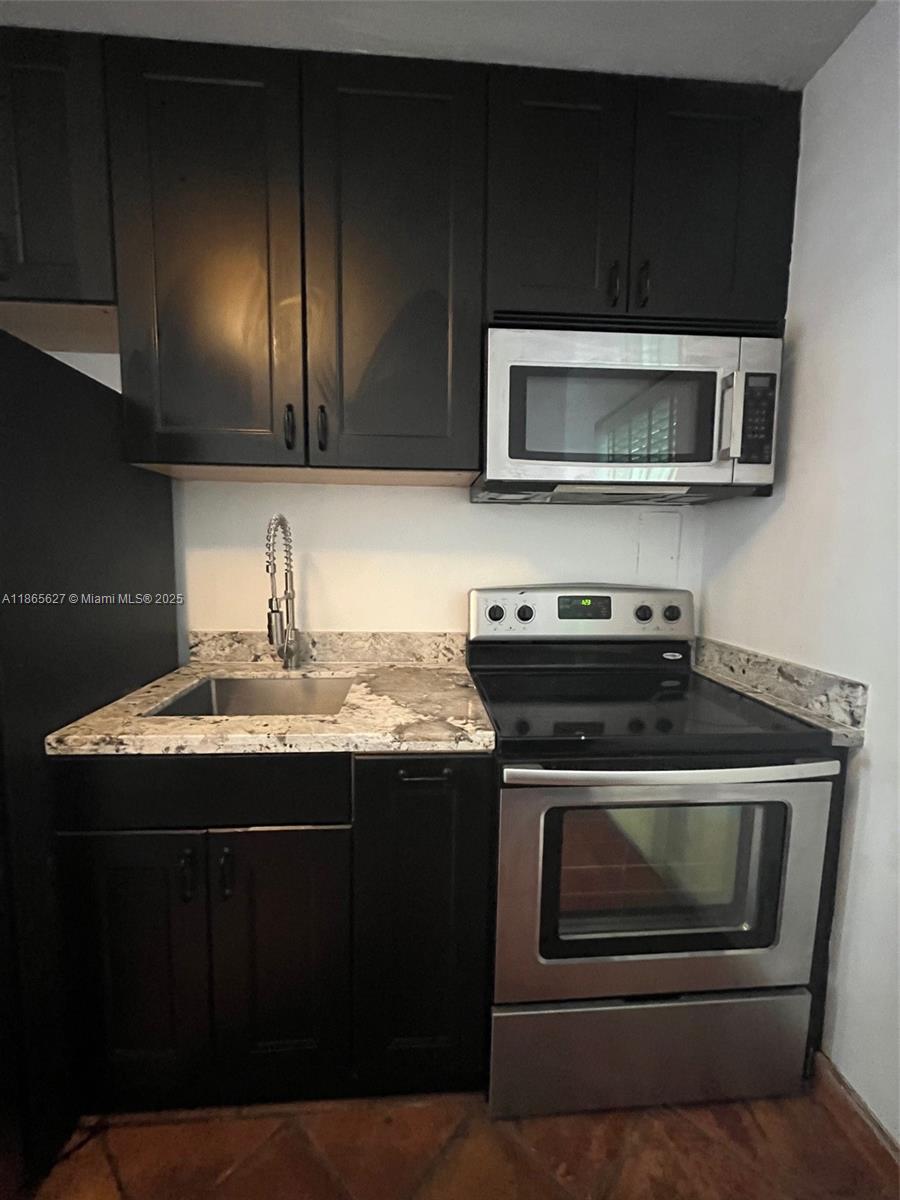 A small kitchen features dark cabinets, stainless steel appliances, and a granite countertop — 645 NE 77th St # 6, Miami FL 33138, MIAMI, FL