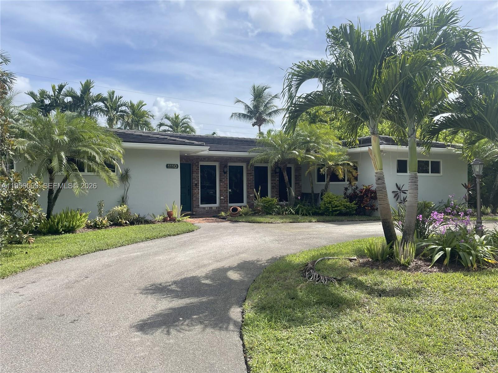A single-story house with a curved driveway, palm trees, and a brick-accented entryway — 1110 Redbird Ave, Miami Springs FL 33166, MIAMI SPRINGS, FL