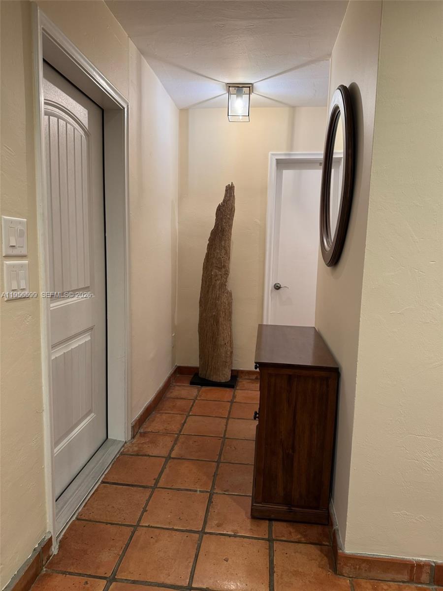 A hallway with terracotta tile flooring, a wooden console table, and a tall driftwood sculpture — 1110 Redbird Ave, Miami Springs FL 33166, MIAMI SPRINGS, FL