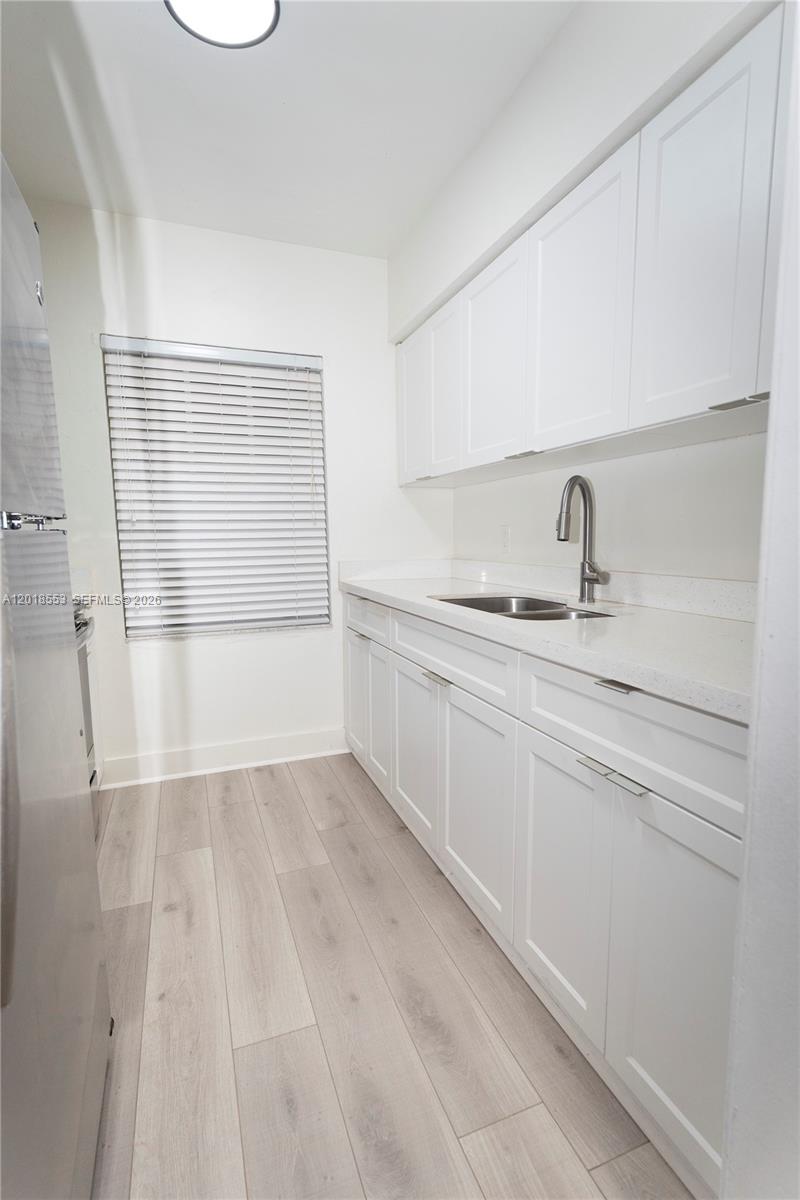 This galley kitchen features white cabinets, light countertops, and wood-look flooring — 111 SW 31st Ct, Miami FL 33135, MIAMI, FL