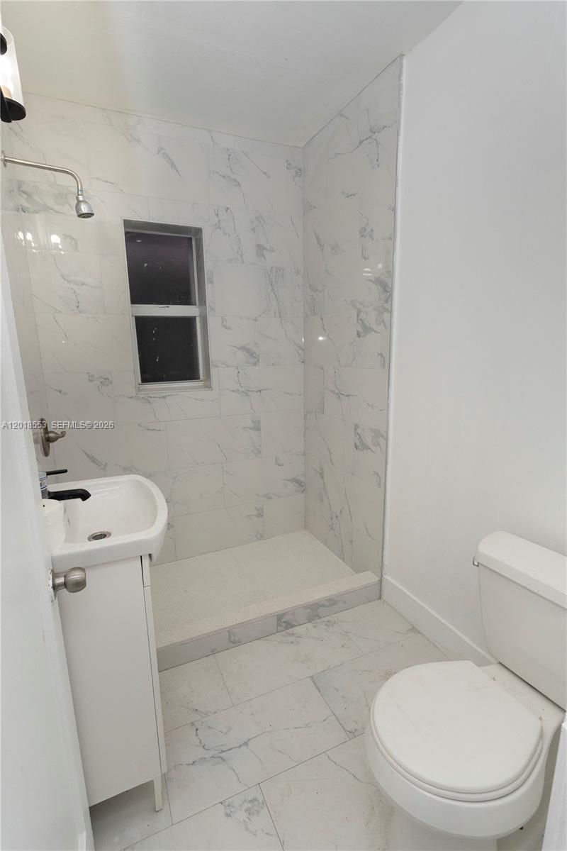 A bathroom features a walk-in shower with white marble-patterned tile, a pedestal sink, and toilet — 111 SW 31st Ct, Miami FL 33135, MIAMI, FL