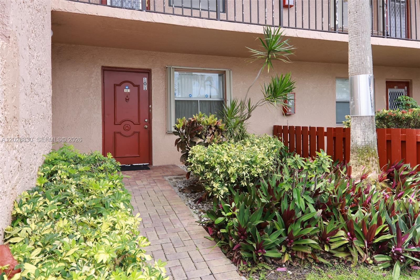 A red front door with the number 101 sits beside a window and landscaping — 7220 Lake Cir Dr # 101, Margate FL 33063, MARGATE, FL