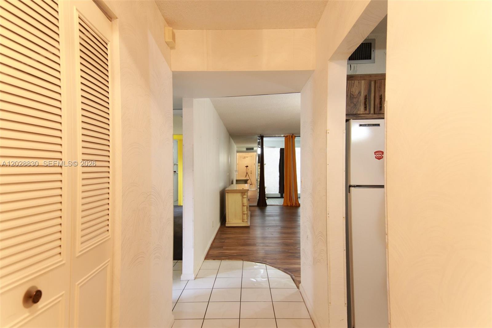 A hallway with white tile flooring leads to a living area with wood-look flooring — 7220 Lake Cir Dr # 101, Margate FL 33063, MARGATE, FL