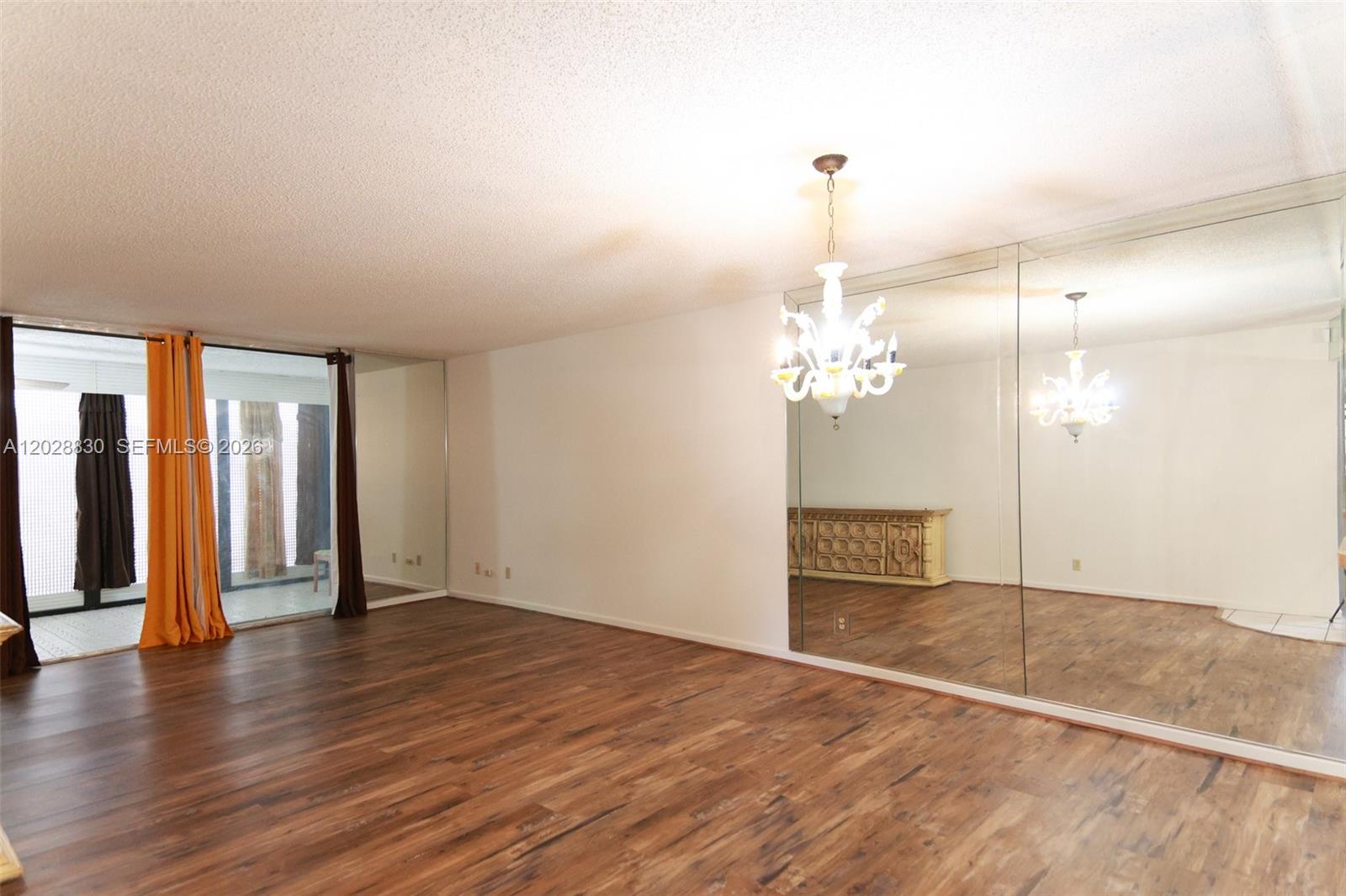 A living room features wood-look flooring, a crystal chandelier, and large wall-to-wall mirrors — 7220 Lake Cir Dr # 101, Margate FL 33063, MARGATE, FL