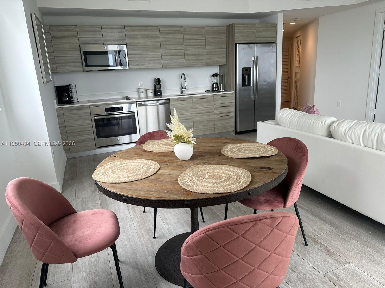 A kitchen with wood-grain cabinets and stainless steel appliances sits behind a round dining table — 121 NE 34th St # 2309, Miami FL 33137, MIAMI, FL
