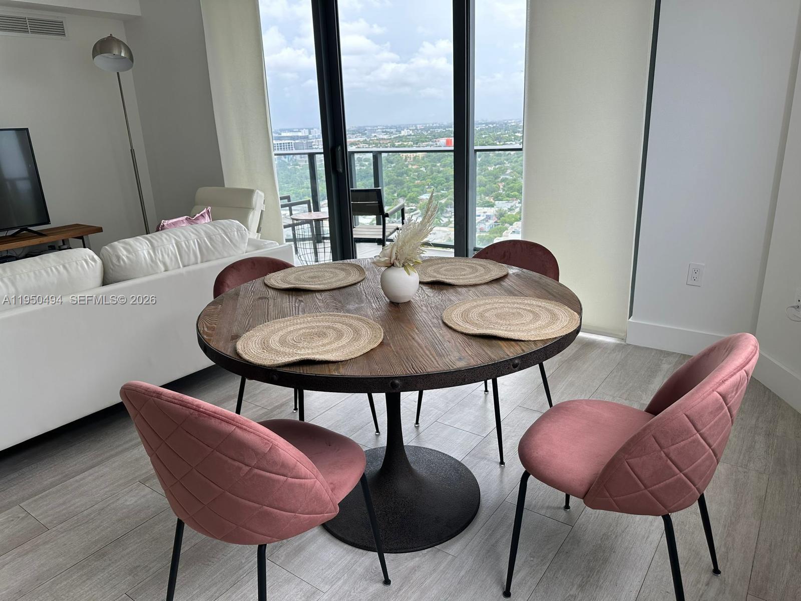 A dining area features a round wooden table with four pink chairs and balcony views — 121 NE 34th St # 2309, Miami FL 33137, MIAMI, FL