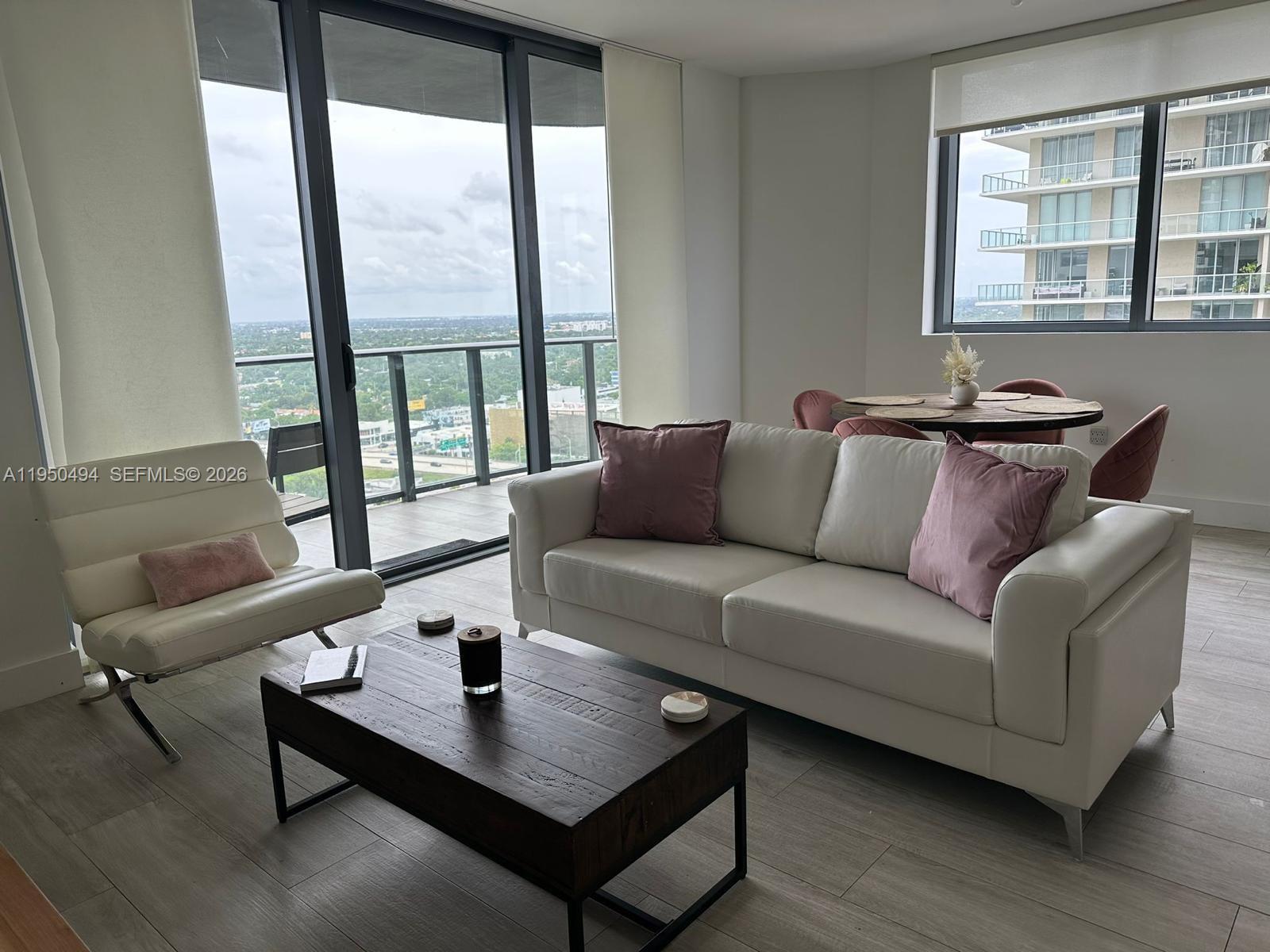A modern living room features a white sofa, a wooden coffee table, and balcony views — 121 NE 34th St # 2309, Miami FL 33137, MIAMI, FL
