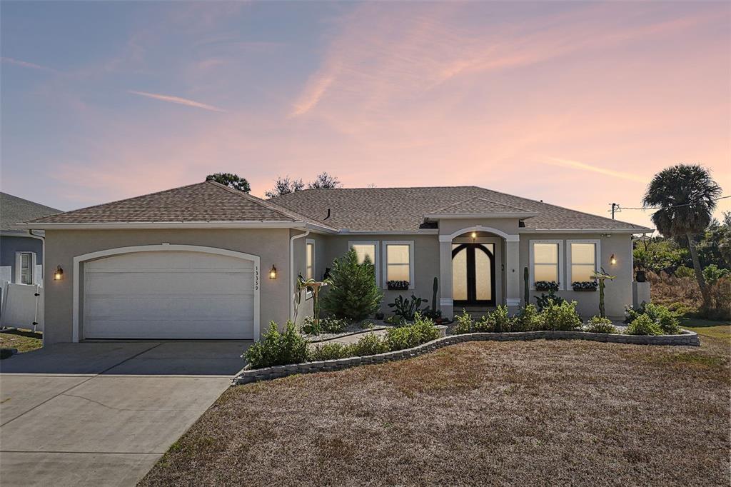 A single-story house with a beige stucco exterior, a two-car garage, and a landscaped yard — 13359 TOLMAN AVENUE, PORT CHARLOTTE, FL