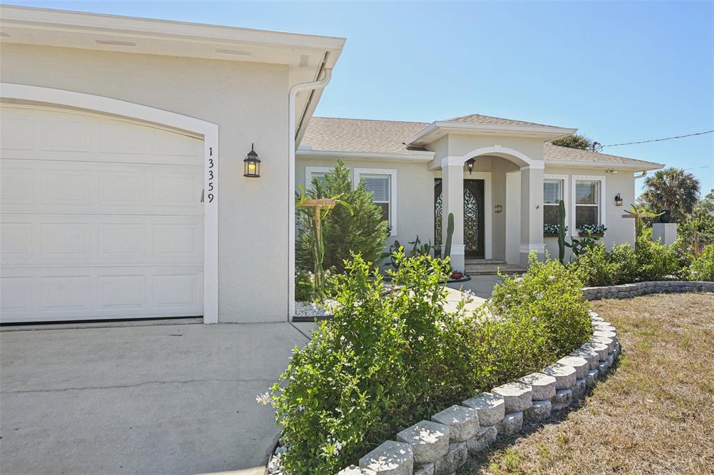 A single-story house with a white garage, arched entryway, and a stone-bordered garden bed — 13359 TOLMAN AVENUE, PORT CHARLOTTE, FL