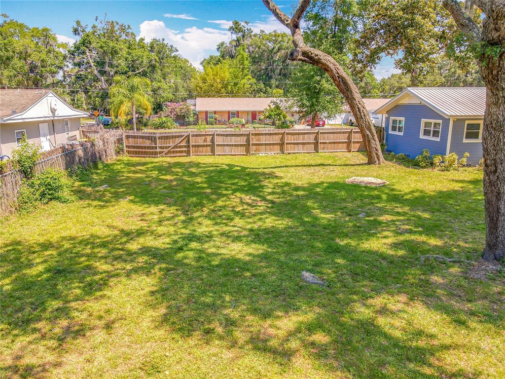 A grassy backyard features a wooden fence, a large tree, and neighboring houses — 1006 E 11TH AVENUE, MOUNT DORA, FL
