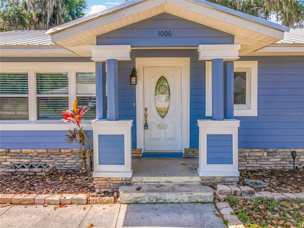 A blue house exterior features a white front door with a decorative oval glass insert — 1006 E 11TH AVENUE, MOUNT DORA, FL