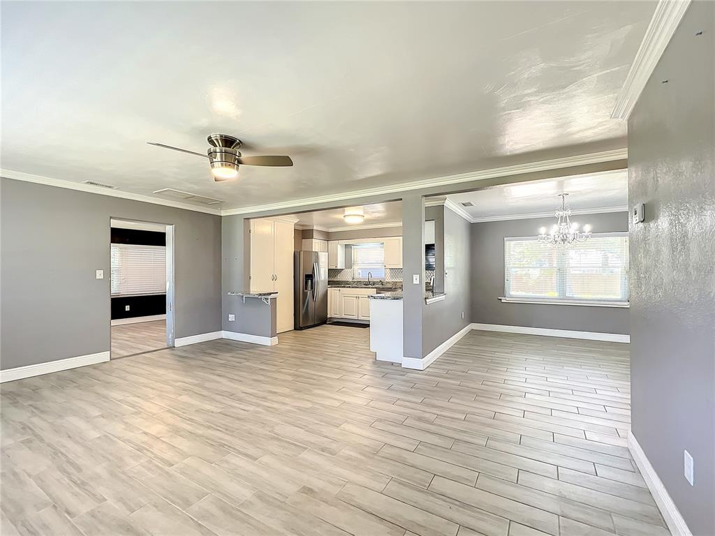 An open-concept living area with gray walls, wood-look tile flooring, and a view into the kitchen — 1006 E 11TH AVENUE, MOUNT DORA, FL