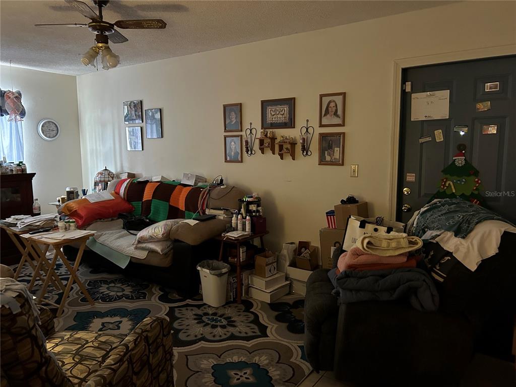 A living room features a sofa, patterned area rug, ceiling fan, and a dark entry door — 5405 1ST STREET NE, ST PETERSBURG, FL
