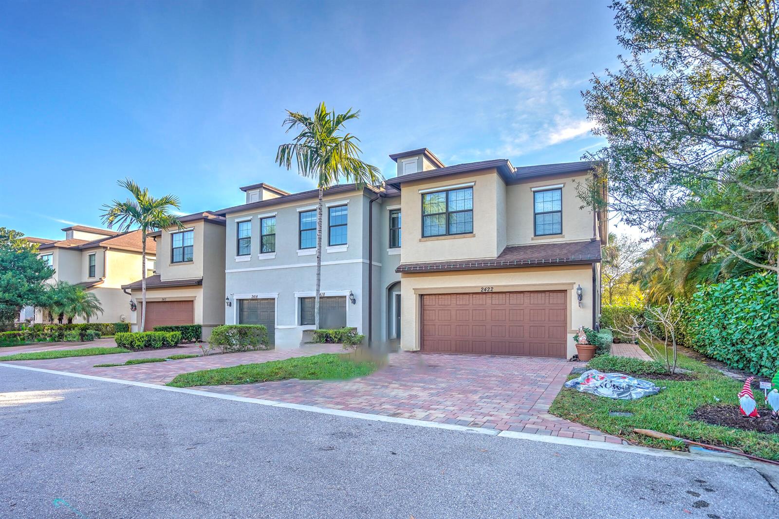 A row of three two-story townhouses with brown garage doors and paved driveways — PALM SPRINGS, FL
