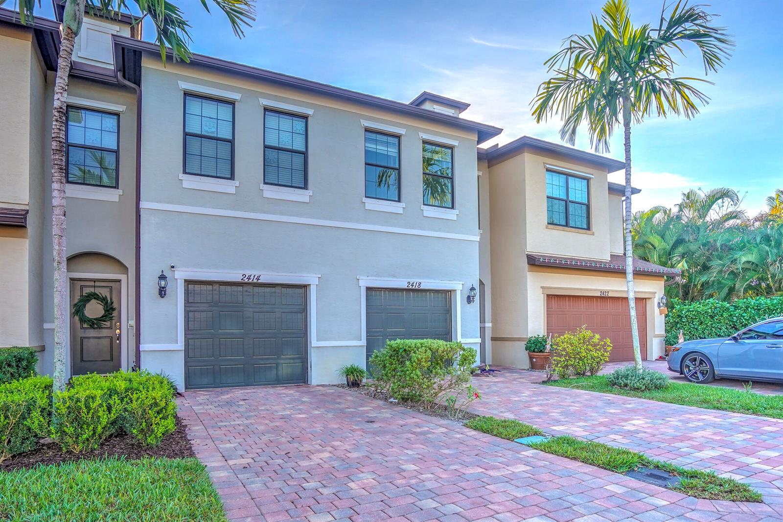 A row of two-story townhomes with paved driveways, garage doors, and palm trees — PALM SPRINGS, FL