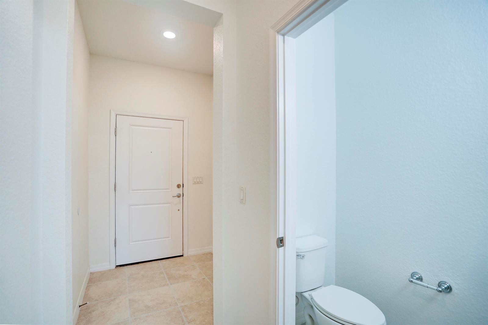 A tiled entryway with a white door leads to a small bathroom with a toilet — PALM SPRINGS, FL