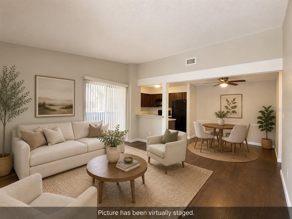A living room and dining area with neutral furniture, wood floors, and a kitchen pass-through — 2942 ANTIQUE OAKS CIRCLE UNIT 88, WINTER PARK, FL