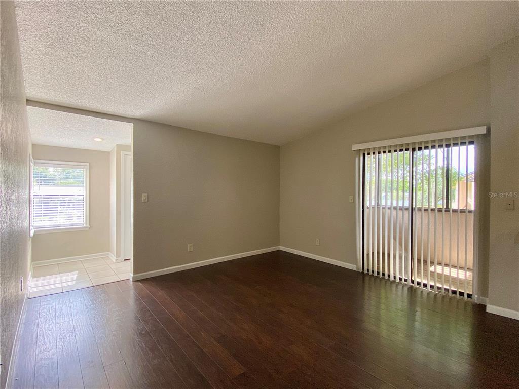 An empty living room features dark wood flooring, beige walls, and a sliding glass door — 2942 ANTIQUE OAKS CIRCLE UNIT 88, WINTER PARK, FL