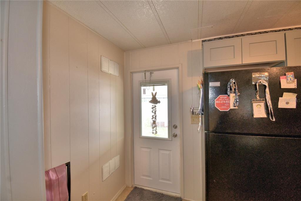 A kitchen area features a black refrigerator, a white exterior door, and light-colored paneled walls — 4918 ROSEWOOD STREET, WINTER HAVEN, FL