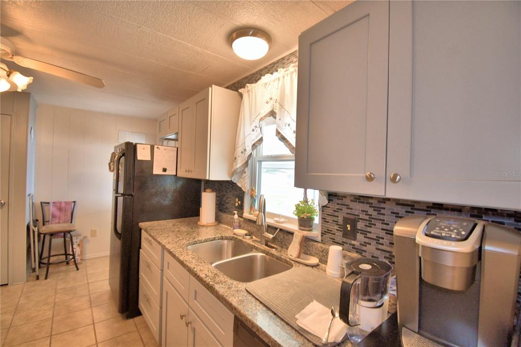 A kitchen features gray cabinets, granite countertops, a double sink, and a black refrigerator — 4918 ROSEWOOD STREET, WINTER HAVEN, FL