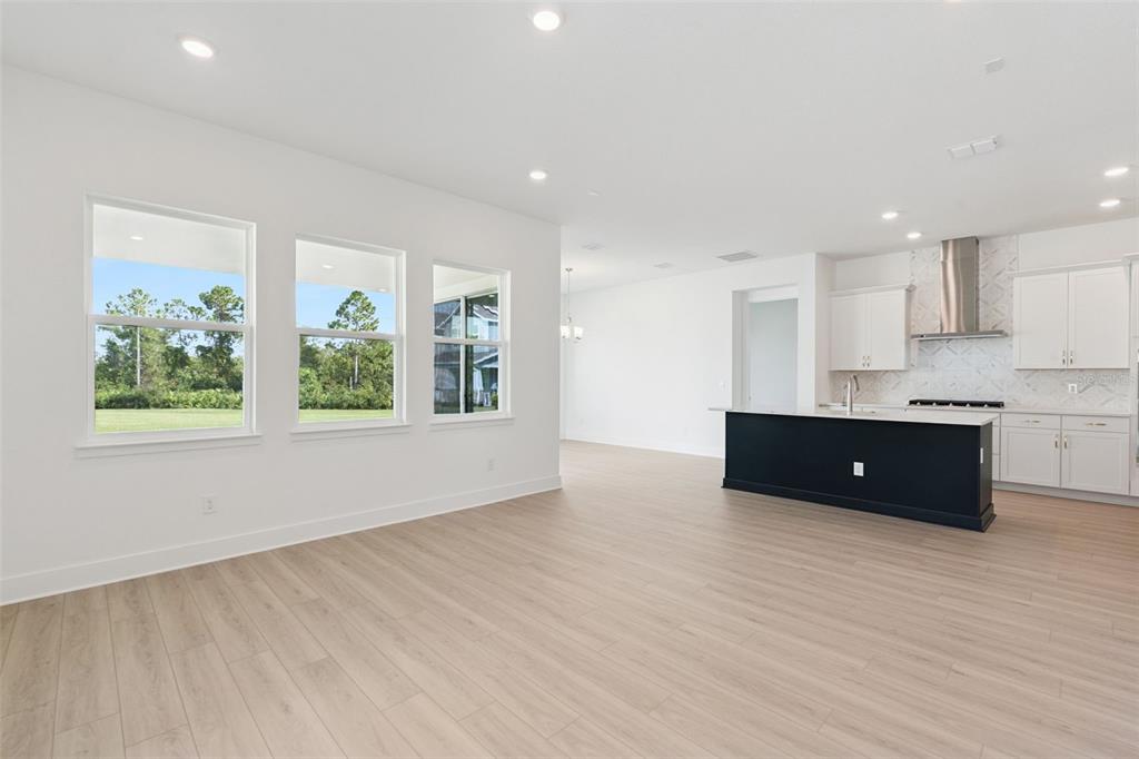 An open-concept kitchen and living area with light wood flooring, white cabinets, and large windows — 17412 HONEYBELL TANGELO COURT, WINTER GARDEN, FL
