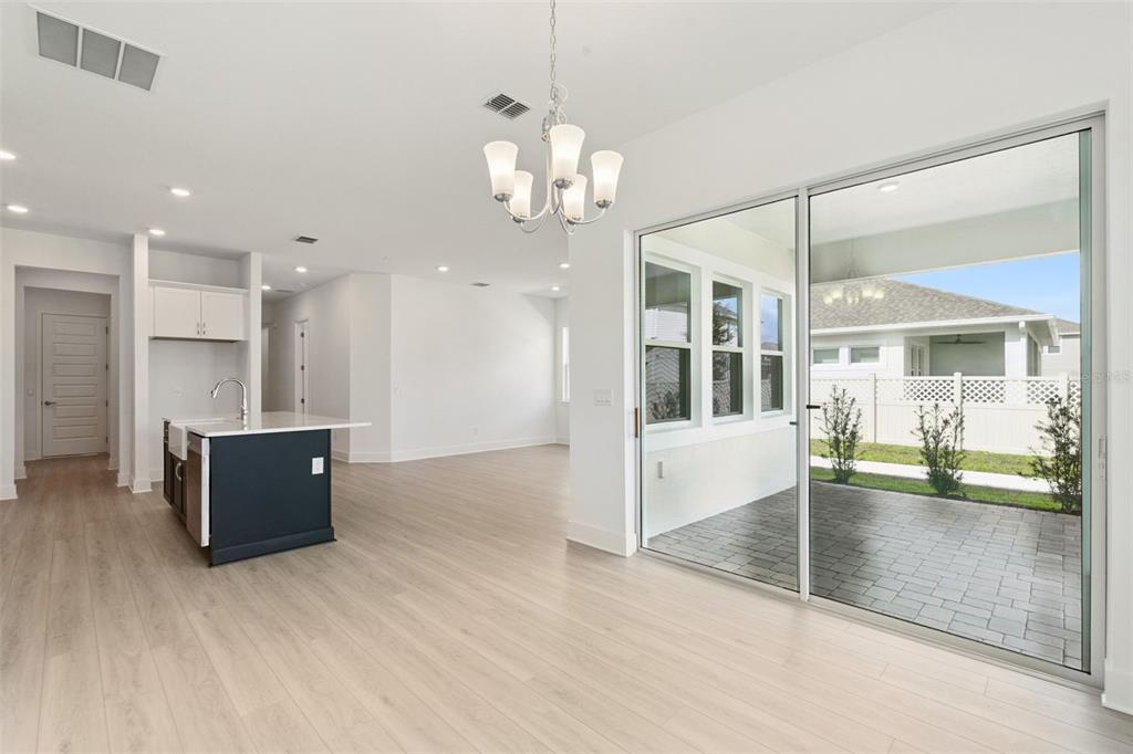 A bright open-concept kitchen and dining area with light wood floors and a sliding glass door — 17412 HONEYBELL TANGELO COURT, WINTER GARDEN, FL