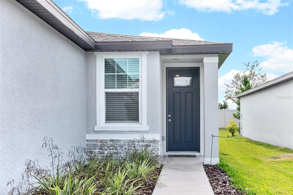 A gray house exterior features a dark front door, a window, and stone veneer accents — 3729 RADIANT MOUNTAIN DRIVE, PLANT CITY, FL